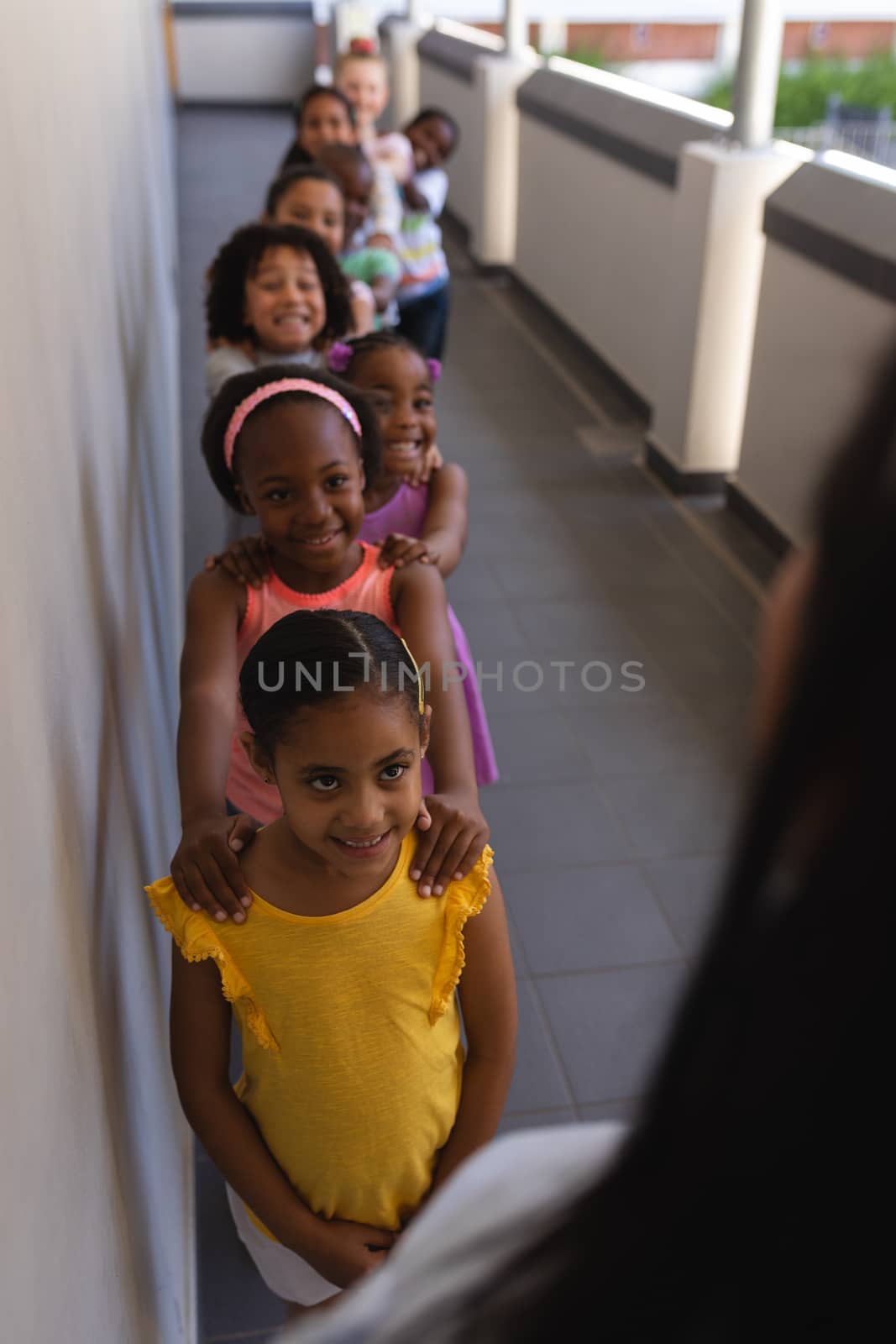 High angle view of schoolkids with teacher standing in row with their hands on shoulder in hallway of elementary school