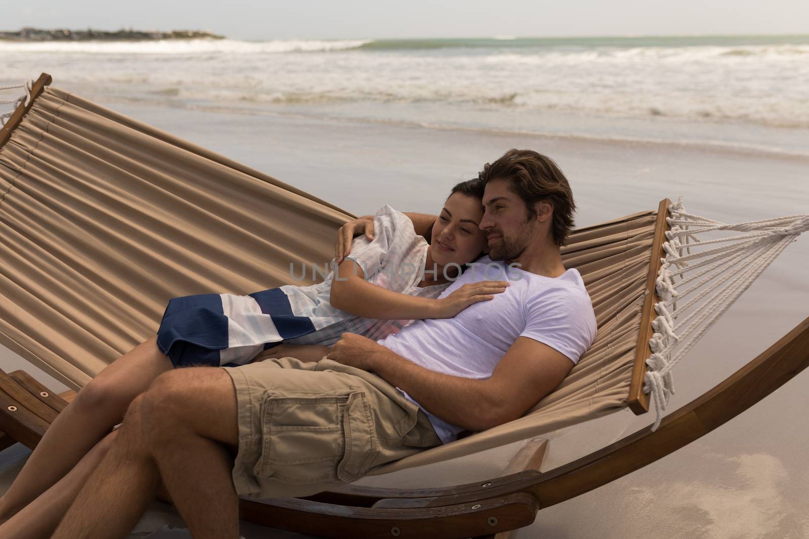 Front view of romantic young couple relaxing on hammock at beach