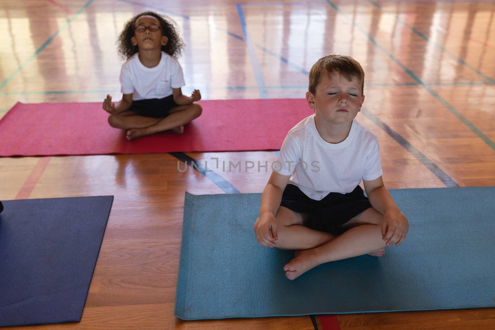 Schoolkids doing yoga and meditating on a yoga mat in school by Wavebreakmedia