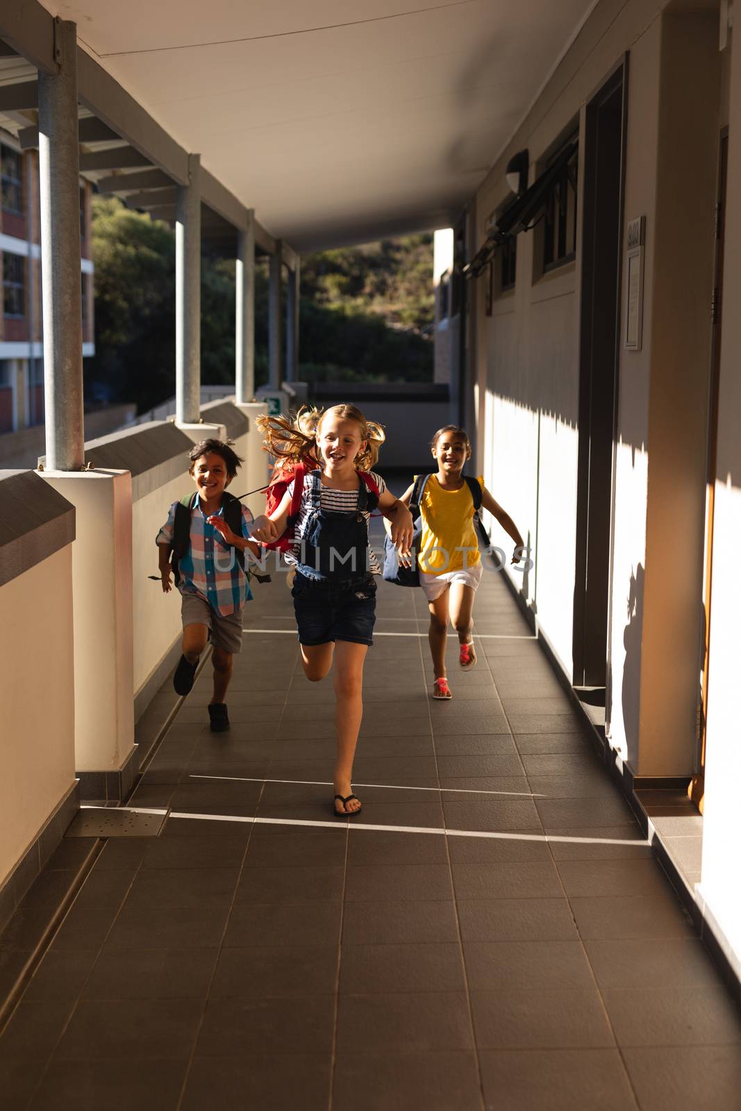 Schoolkids with schoolbags running in hallway by Wavebreakmedia