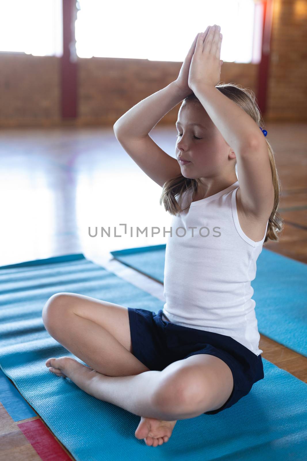 Side view of schoolgirl doing yoga and meditating on a yoga mat in school