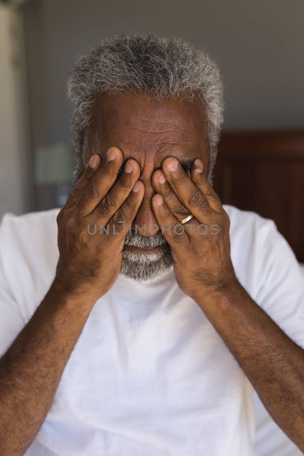 Portrait of a worried senior African American man covering his eyes in bedroom at home