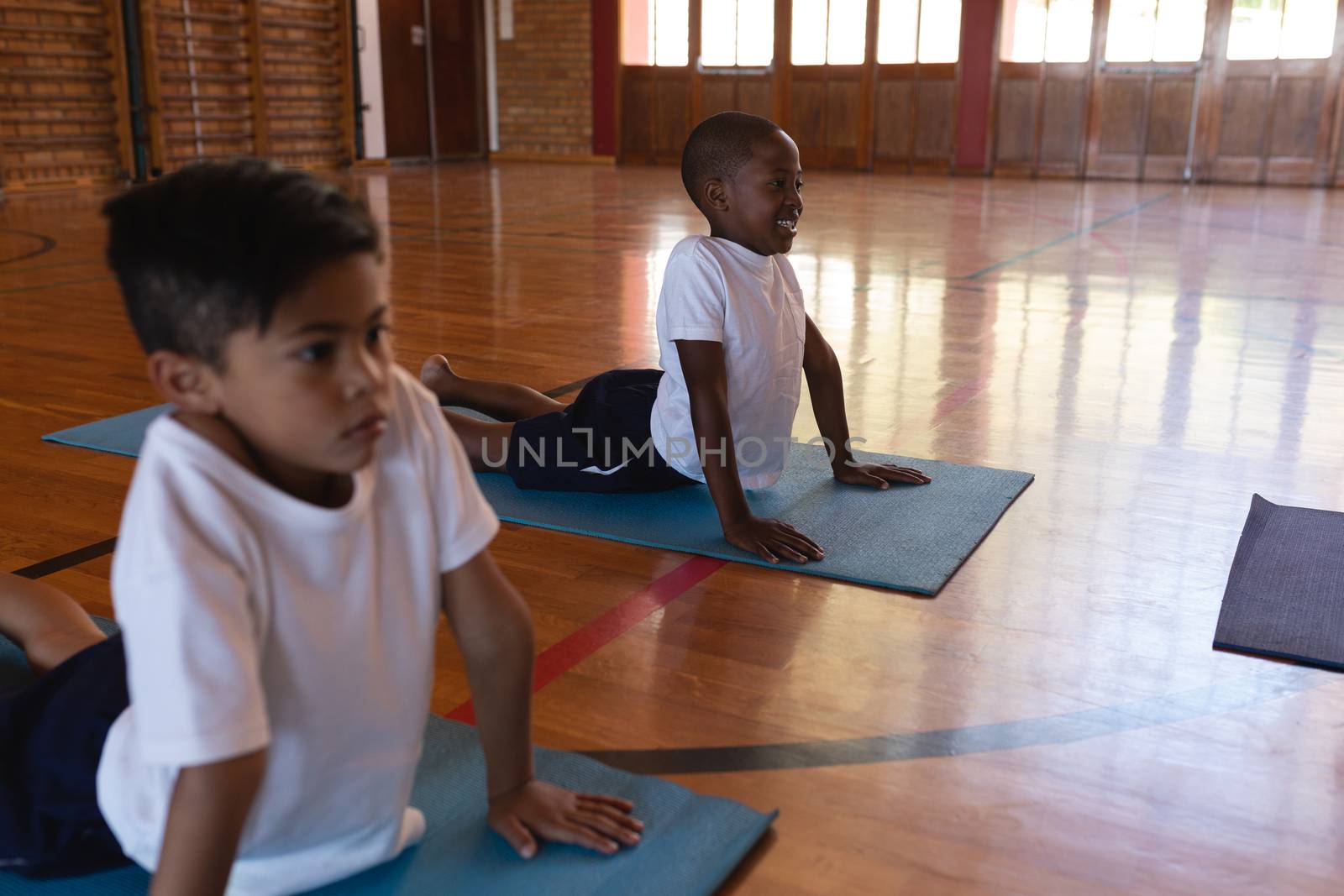 Side view of schoolkids doing yoga position on a yoga mat in school gymnasium 