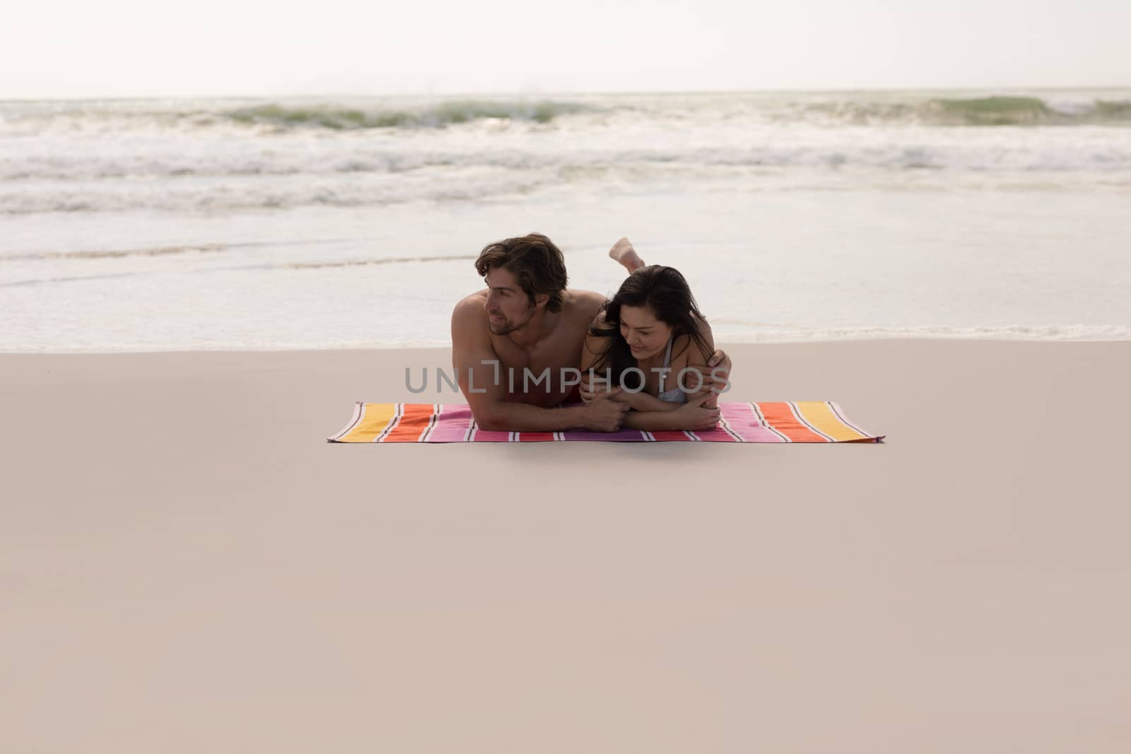 Front view of romantic young couple relaxing on blanket at beach in the sunshine