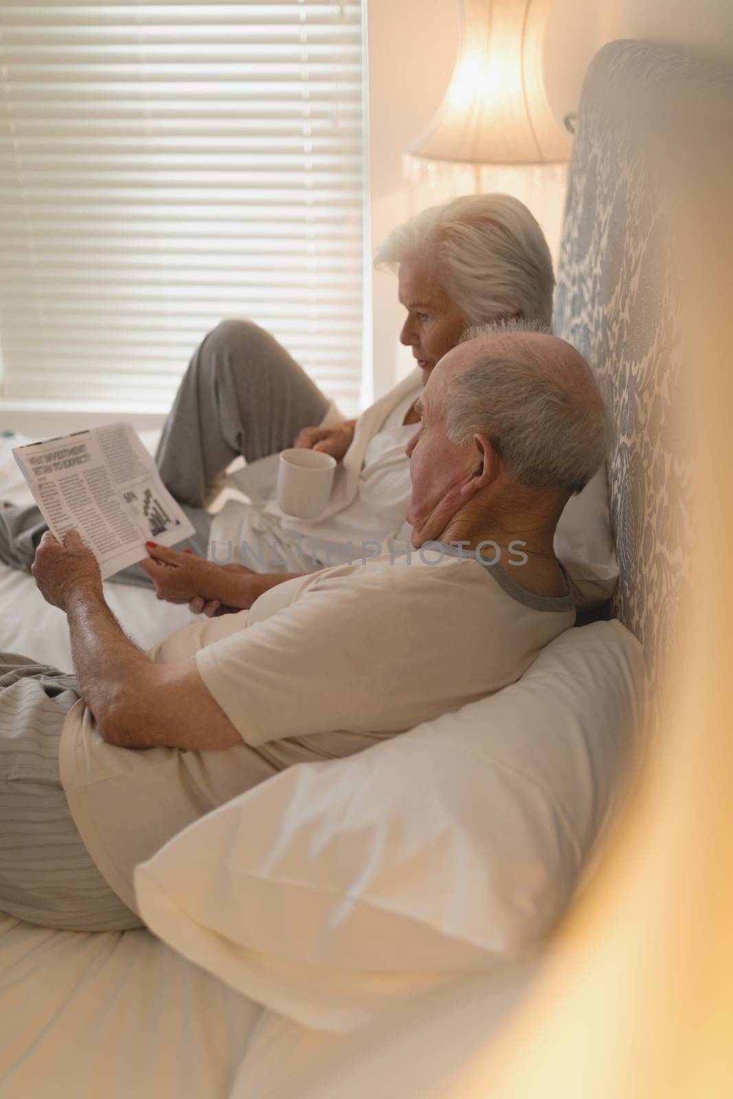Side view of senior couple reading newspaper and drinking on the bed at home