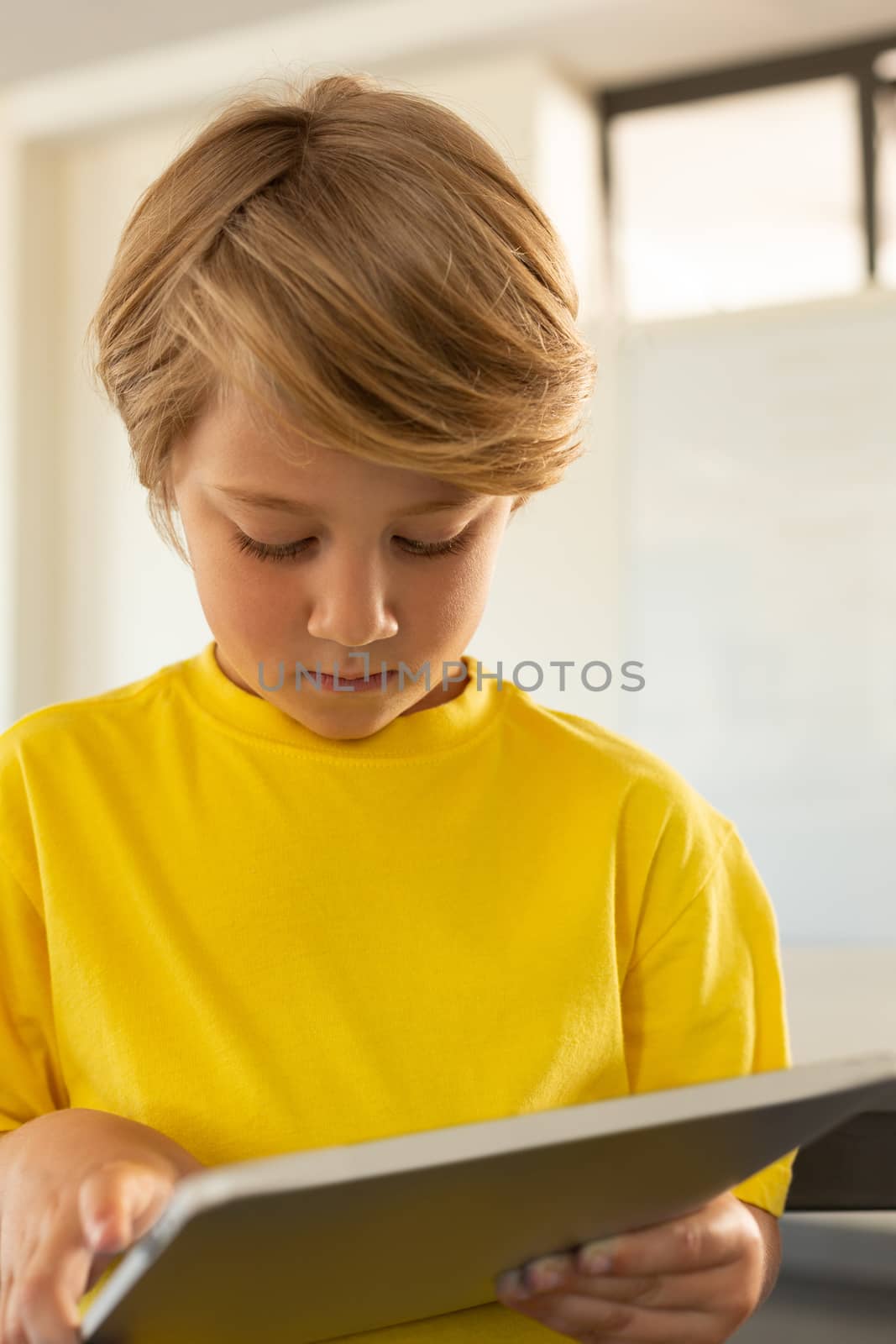 Front view of cute Caucasian boy using digital tablet in a classroom at elementary school