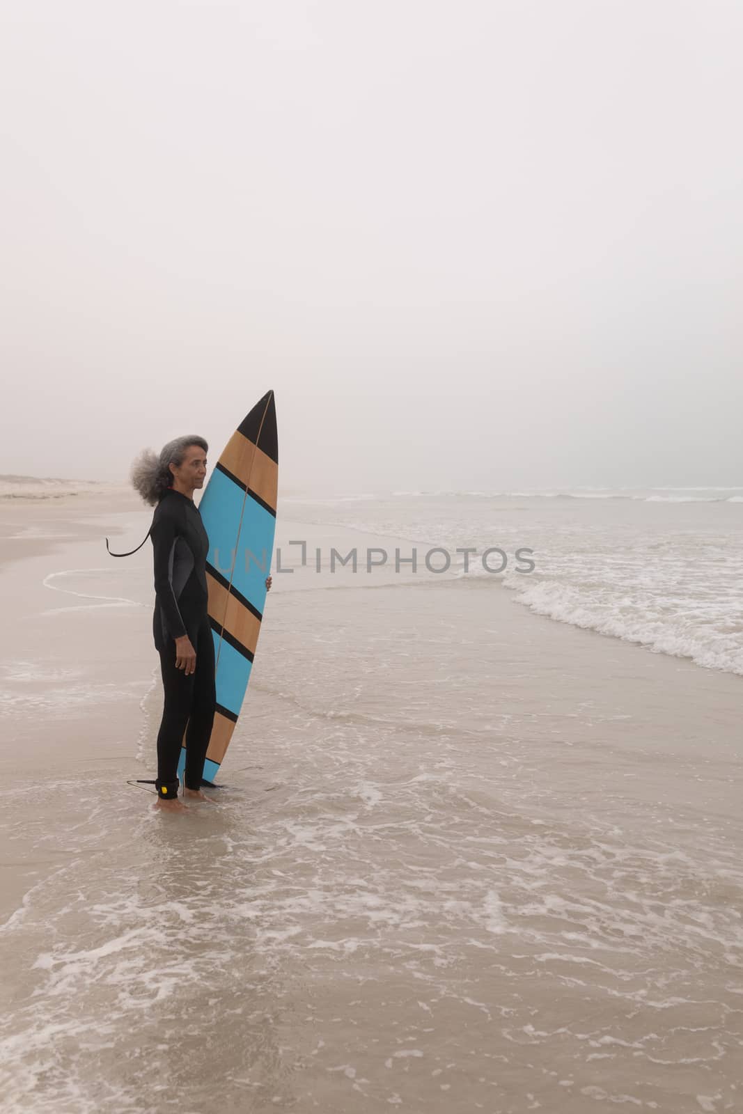 Side view of senior female surfer with surfboard standing on the beach