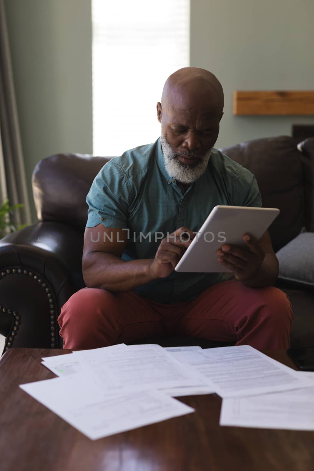 Front view of senior man filling form while using digital tablet in living room at home