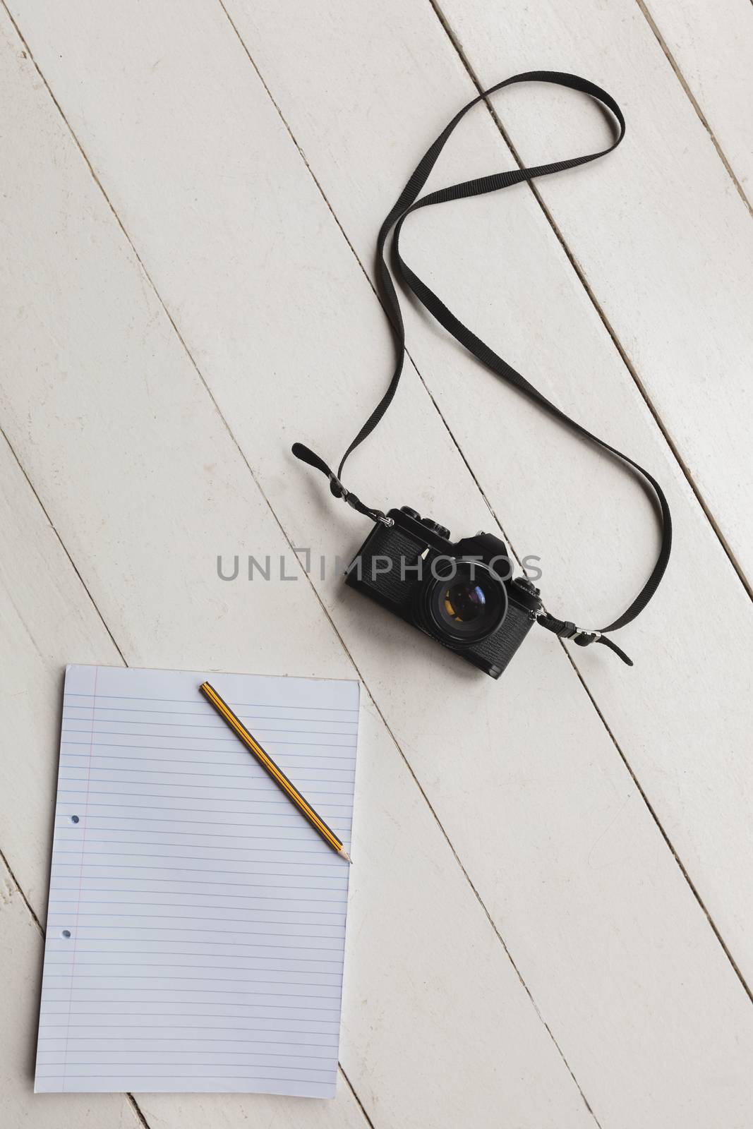 Overhead view of a notepad, pencil and camera placed on the floor at home