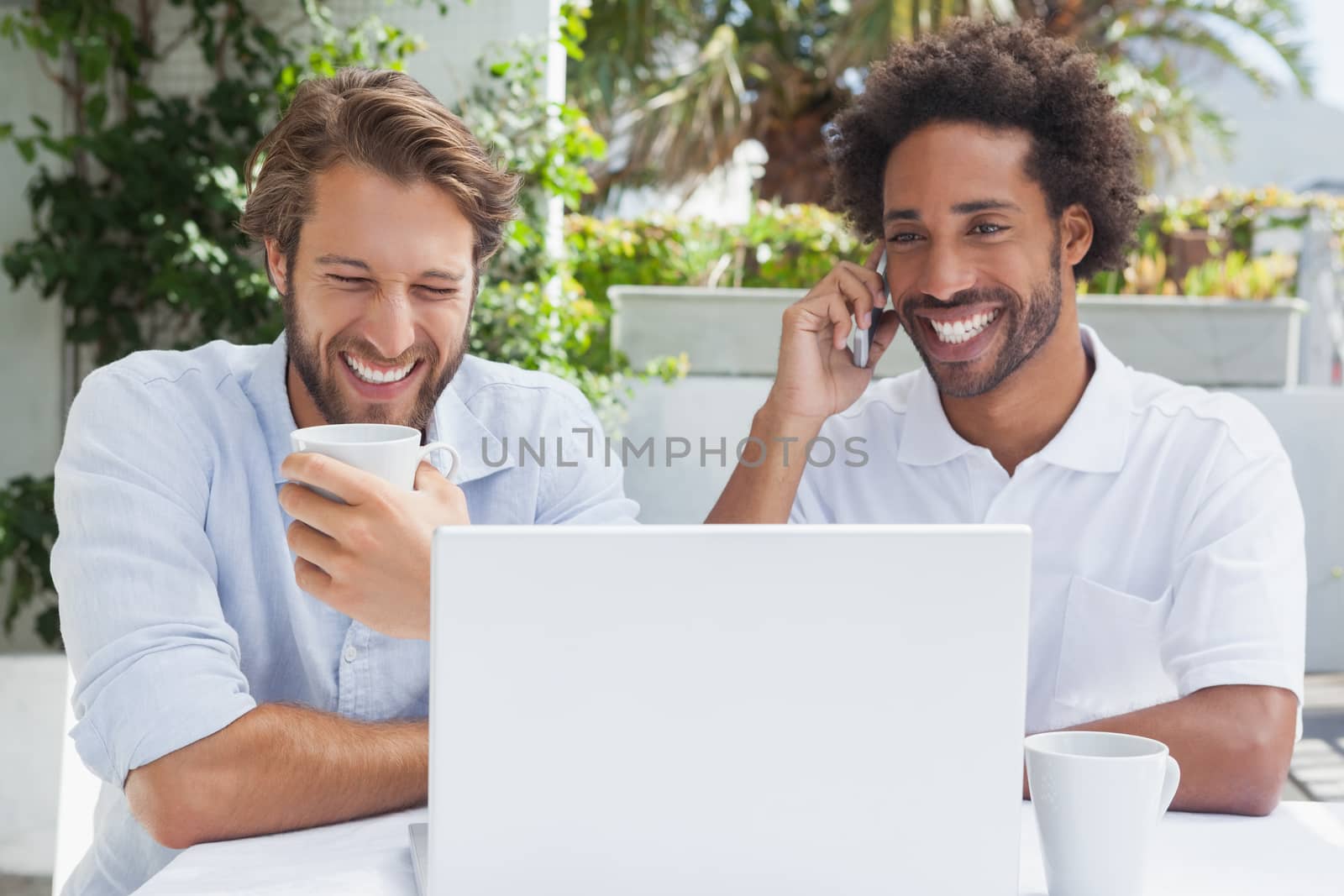 Happy friends enjoying coffee together with laptop outside at the coffee shop