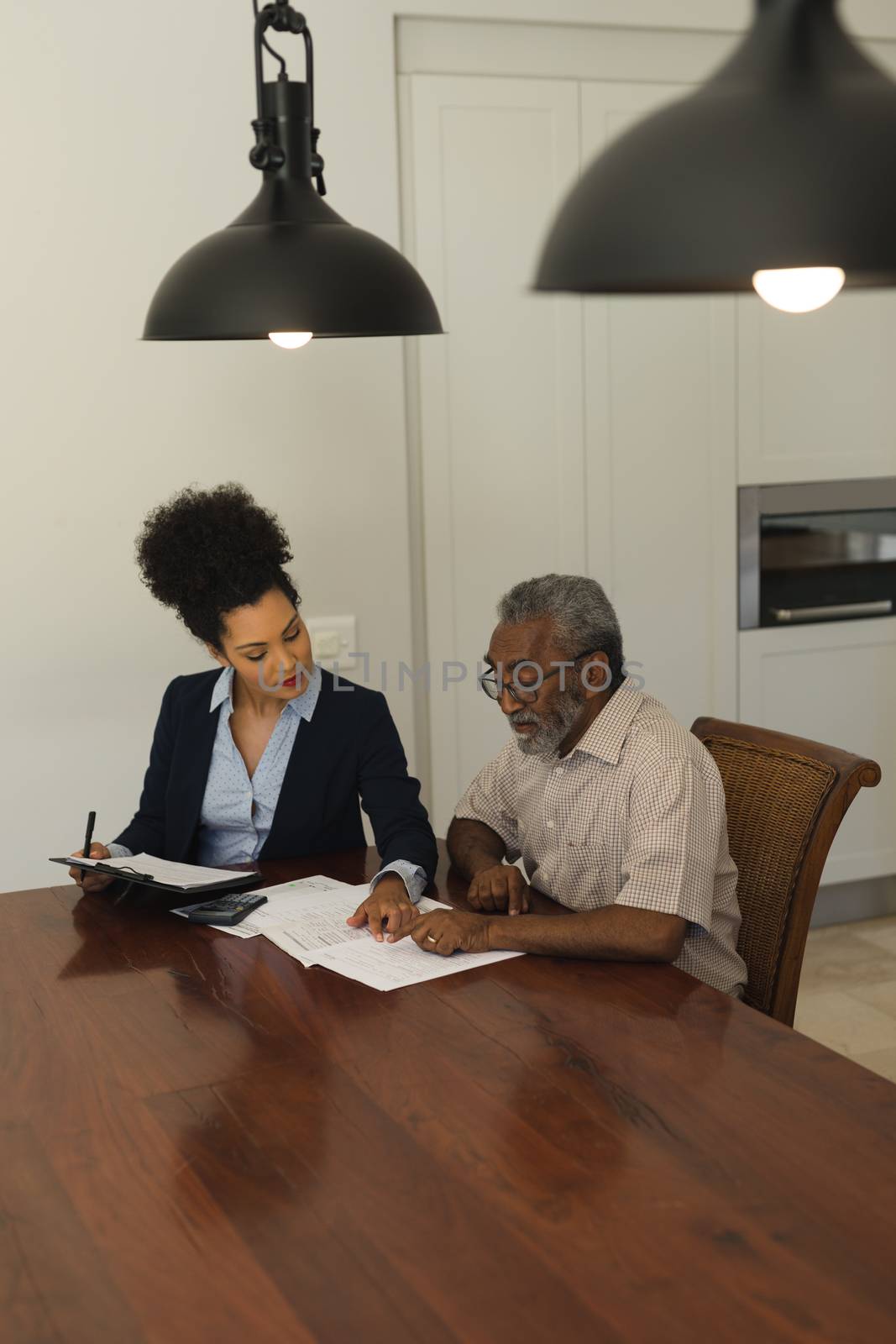 Side view of a senior African American  man and real estate agent discussing over documents on the table in living room at home