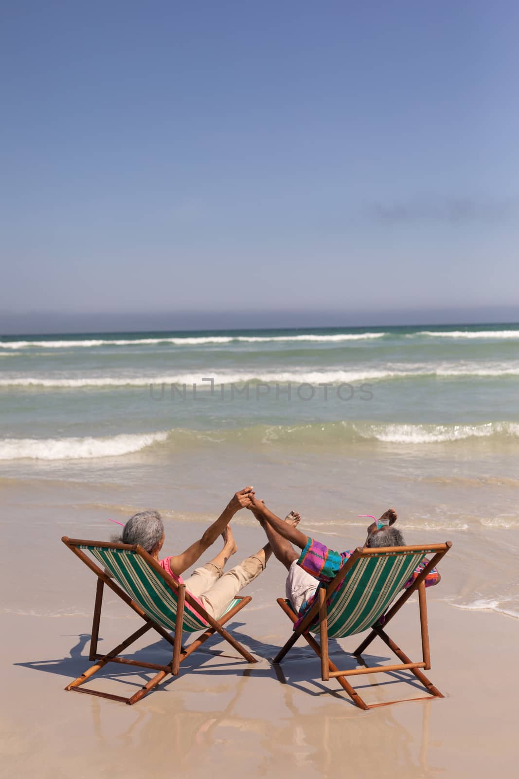 Senior couple relaxing on sun lounger and holding hands on beach by Wavebreakmedia