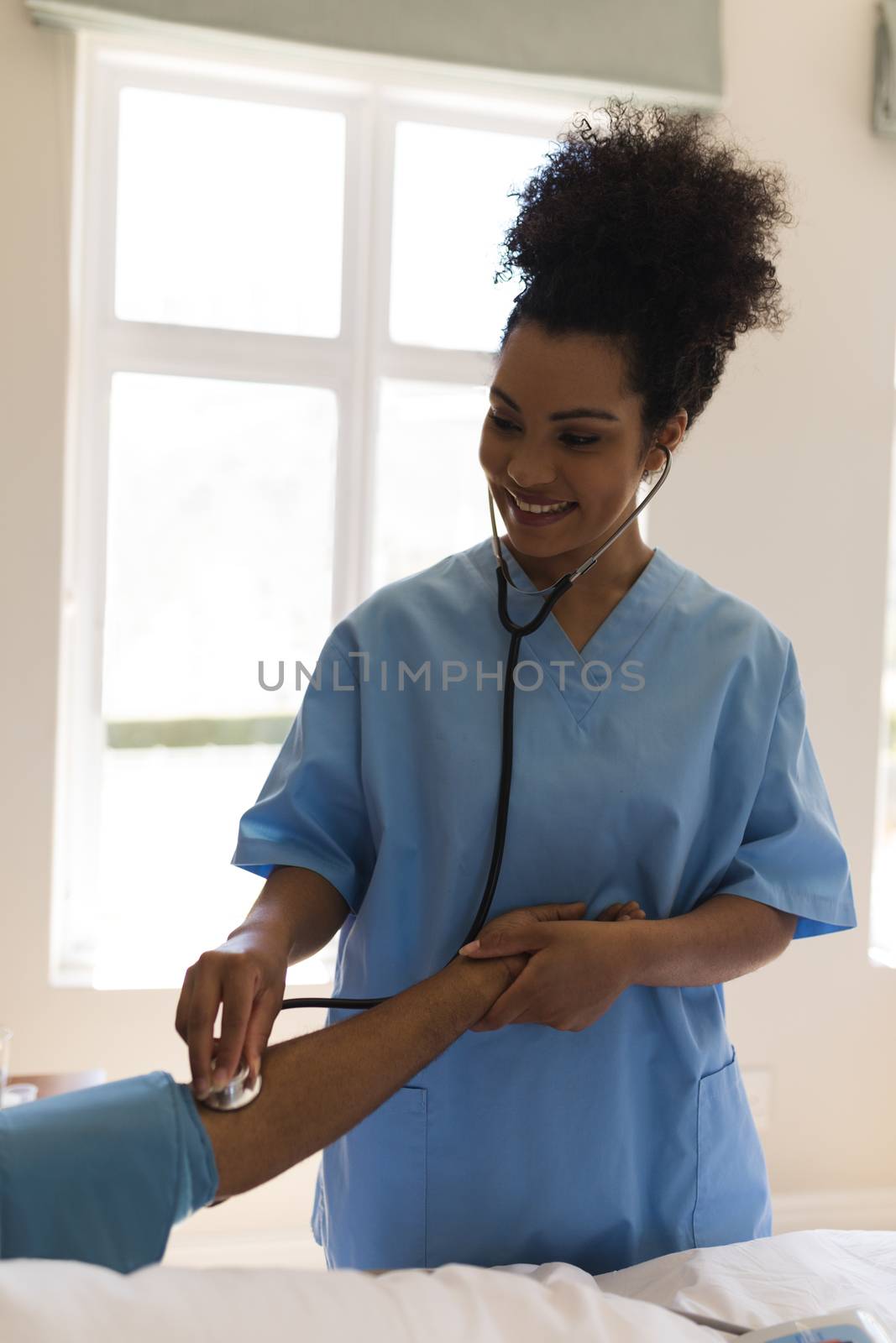 Front view of young pretty African American female doctor measuring blood pressure of senior African American man in bedroom at home