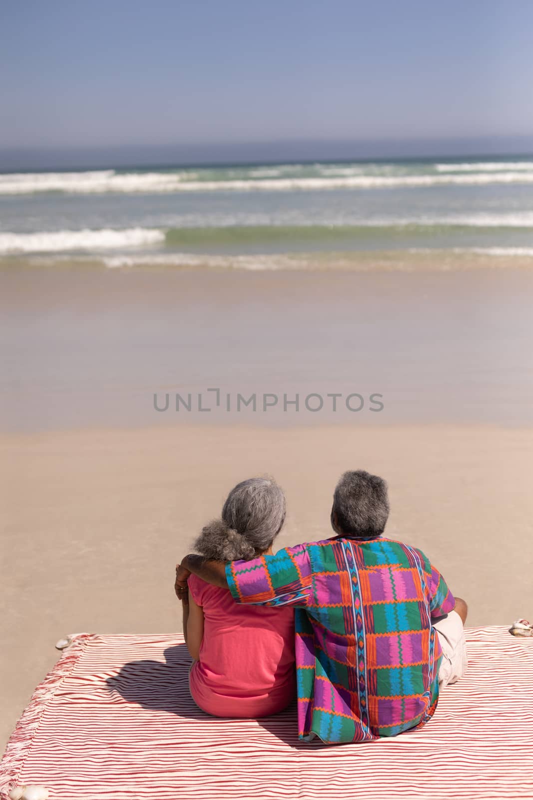 Rear view of senior couple sitting on blanket at beach in the sunshine