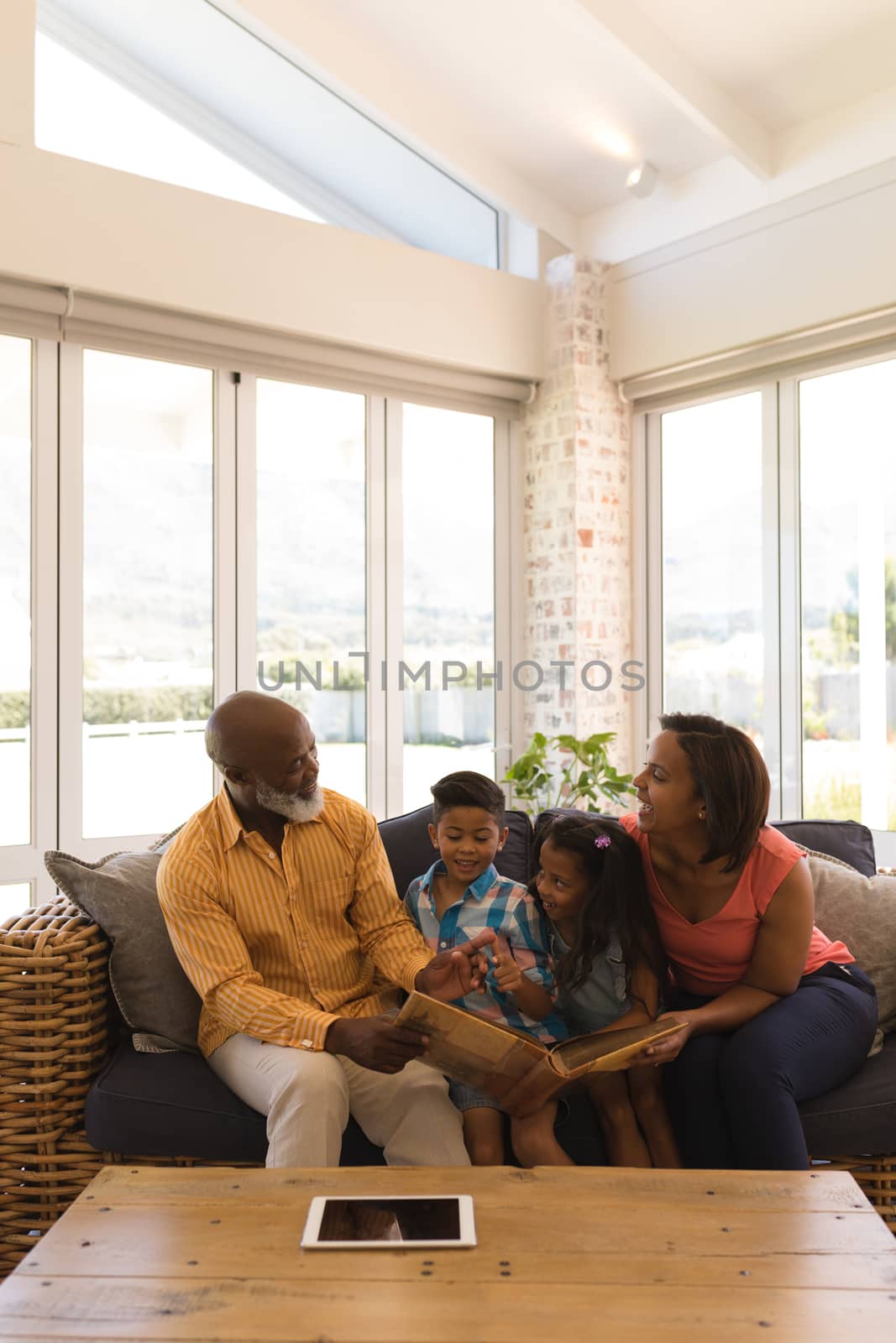 Front view of a happy African American multi-generation family reading a story book while sitting on a wicker sofa in living room at home