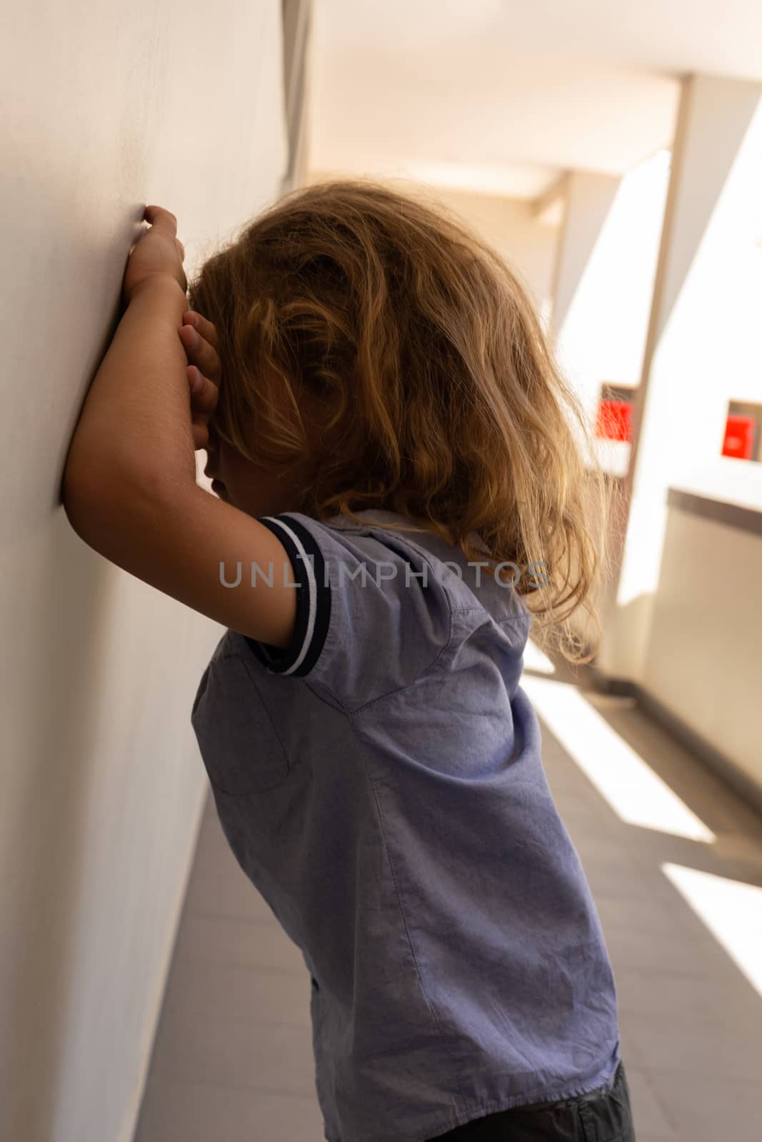 Side view of mixed -race sad schoolgirl leaning against wall in school corridor