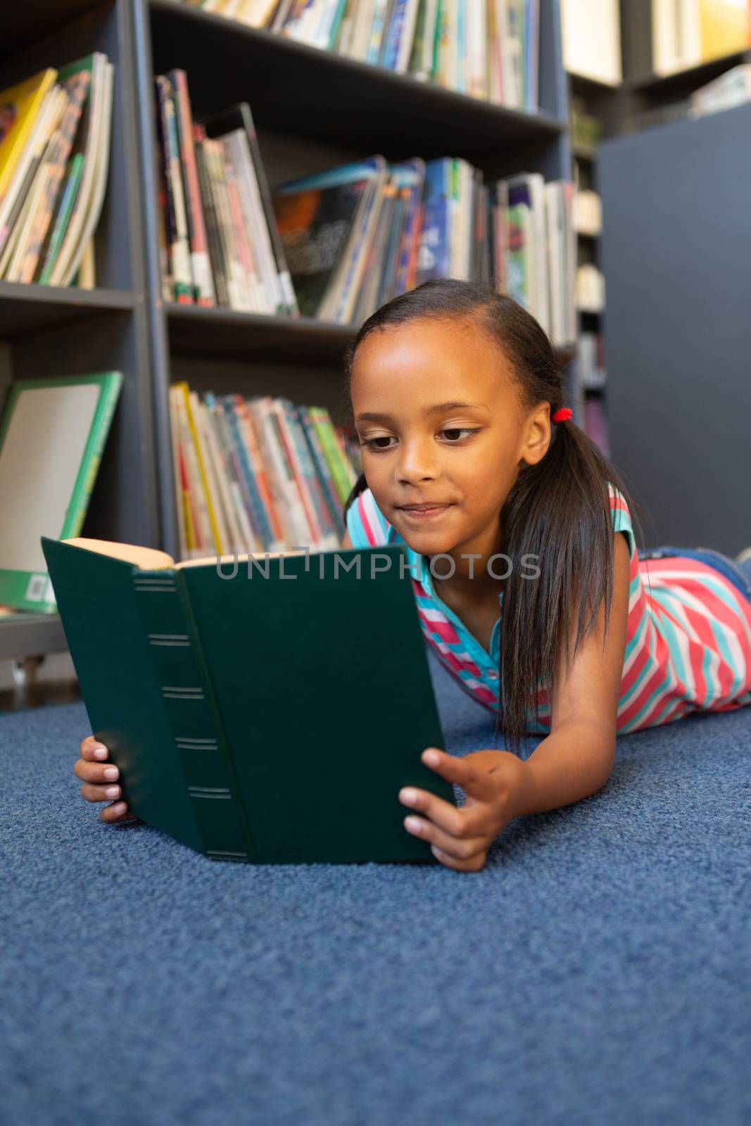 Front view of a mixed-race schoolgirl reading a book in the library at school