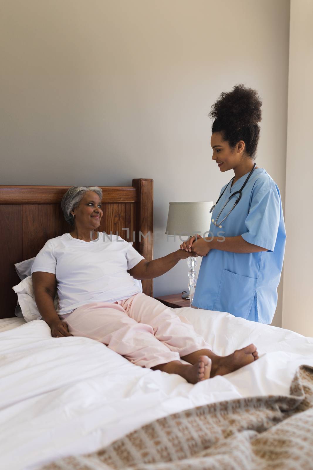 Front view of a young African American female doctor consoling senior African American woman in bedroom at home