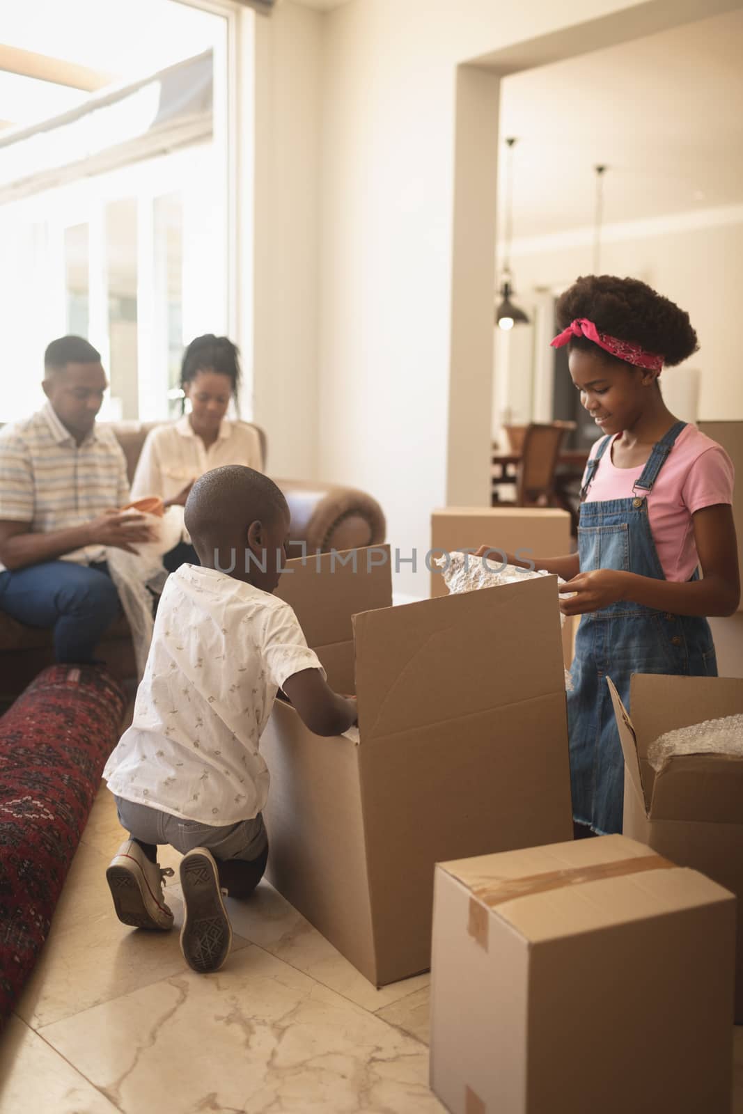 Side view of African American children unpacking their belongings and parents sitting on sofa at home