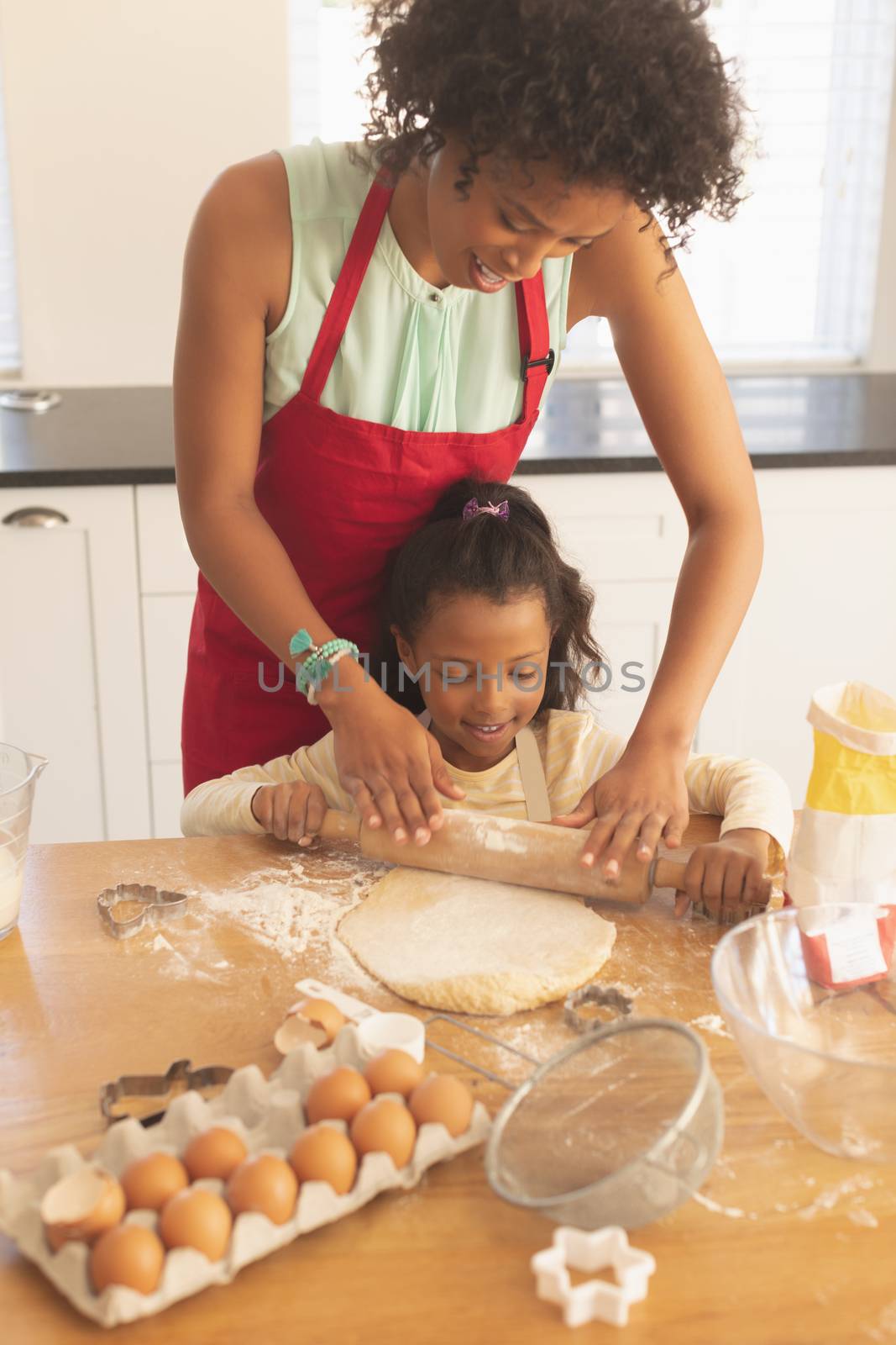 Front view of African American mother and daughter rolling out cookie dough in kitchen at home