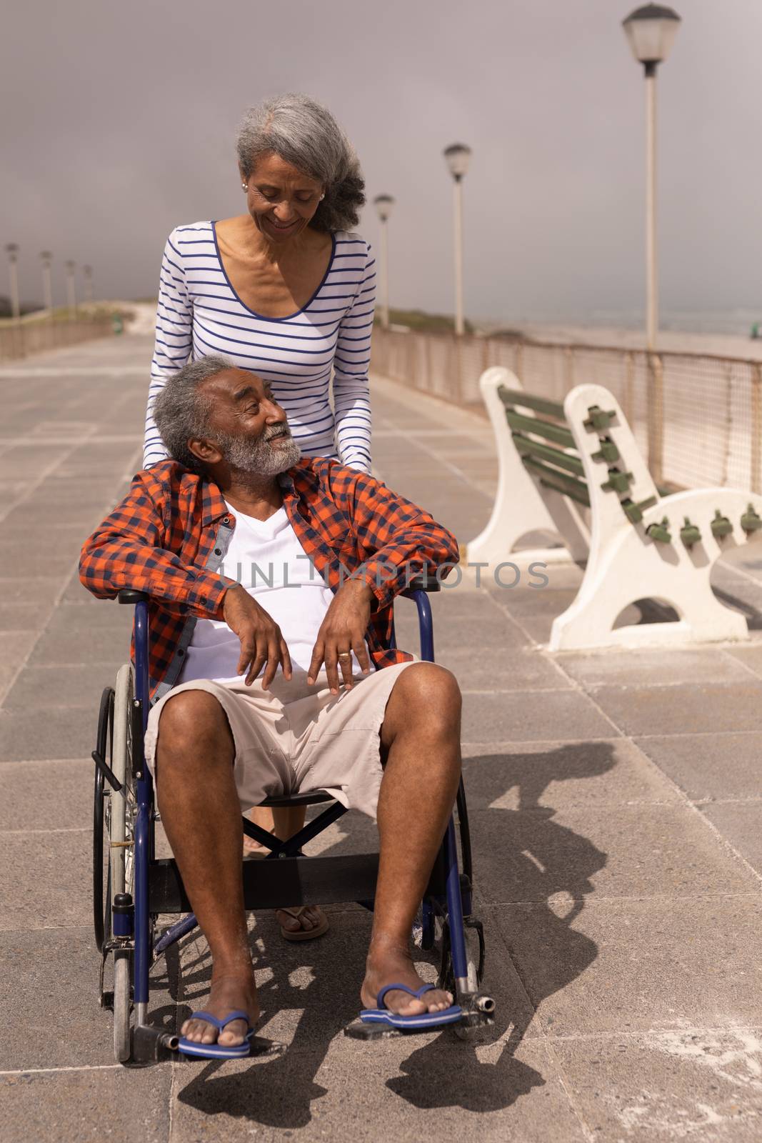 Front view of disabled senior man and senior woman talking with each other on promenade in the sunshine