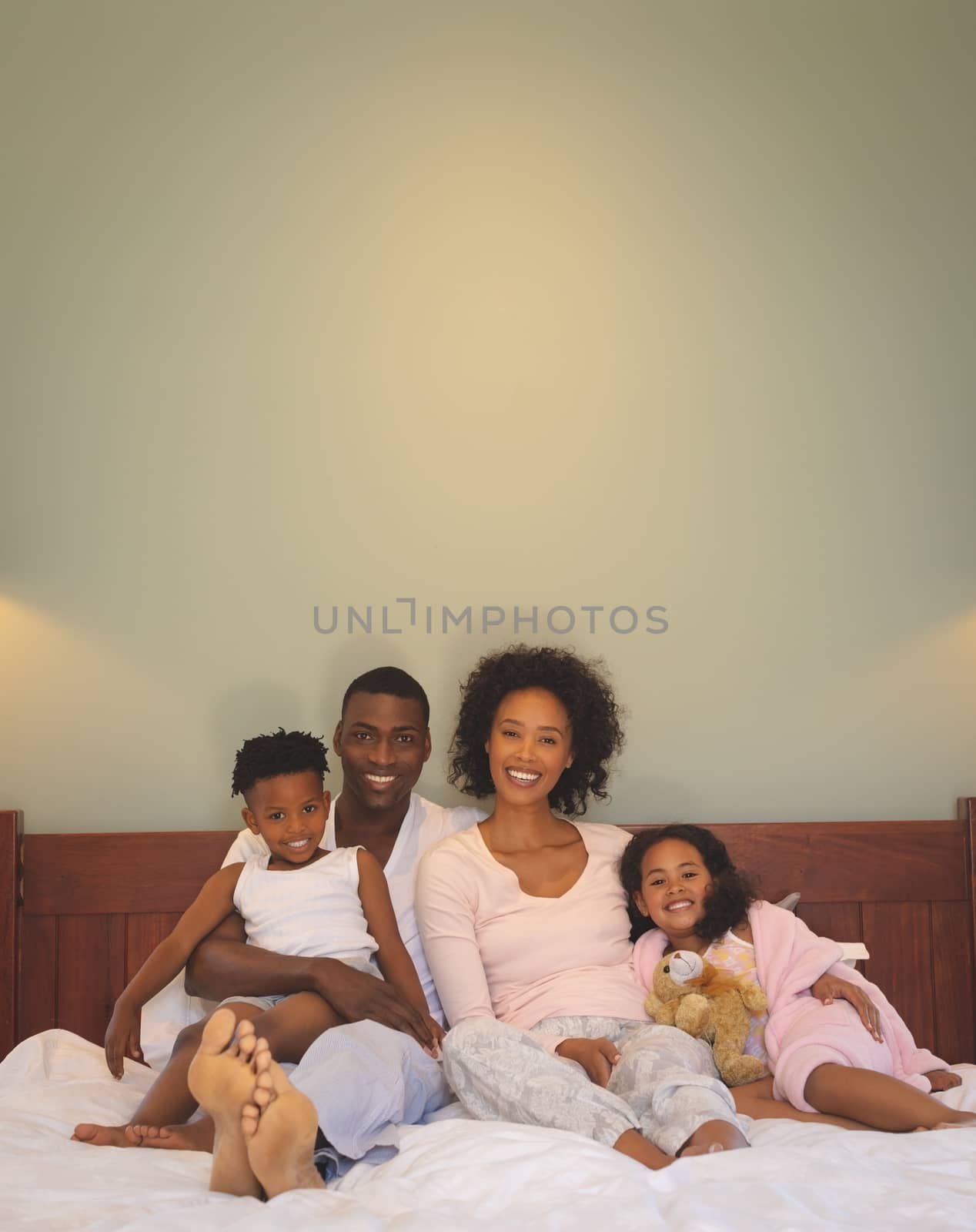 Front view of happy African American family relaxing on bed and looking at camera in a comfortable home