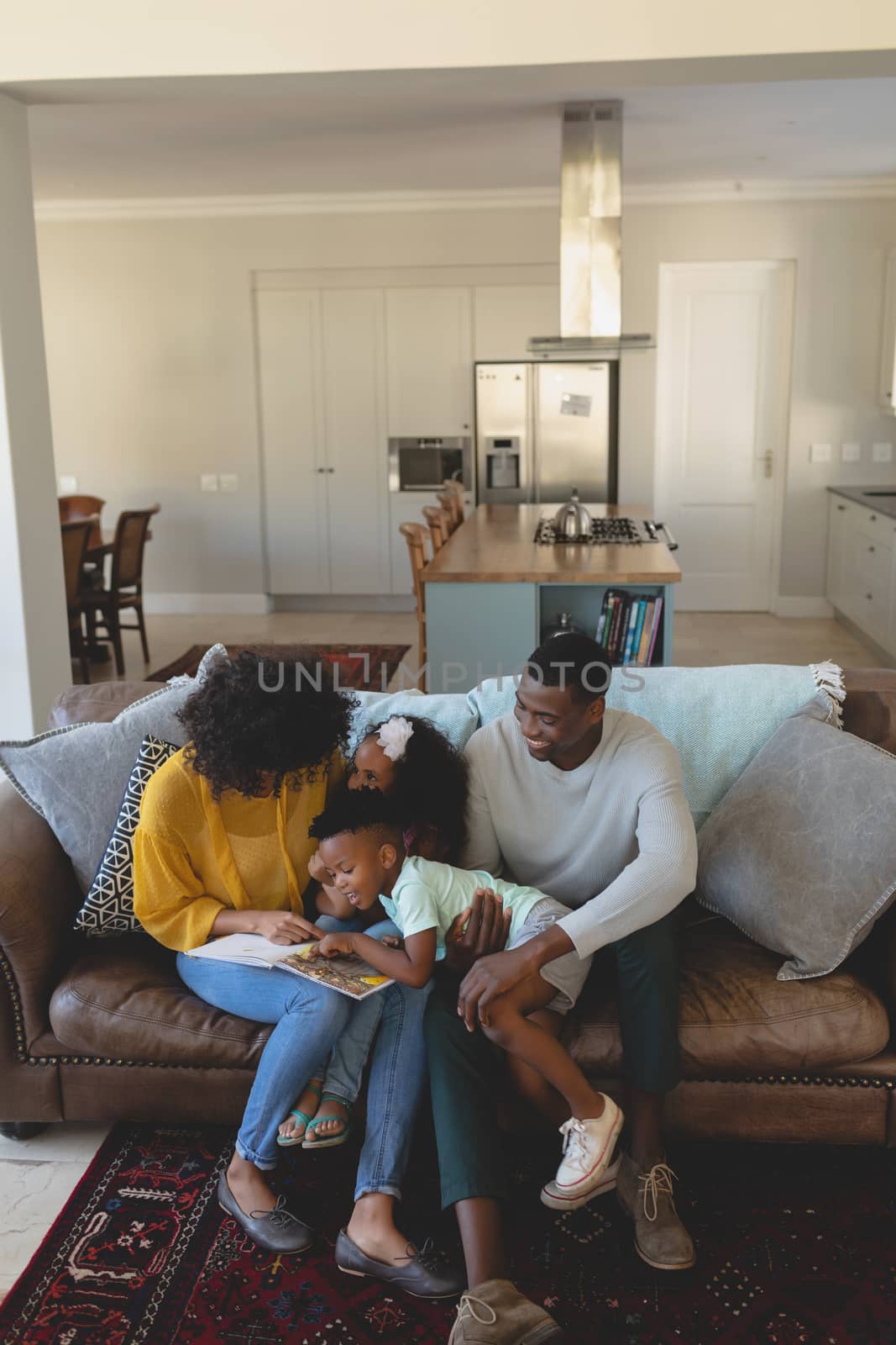 High angle view of happy African American parents with their cute children reading storybook on the sofa in a comfortable home