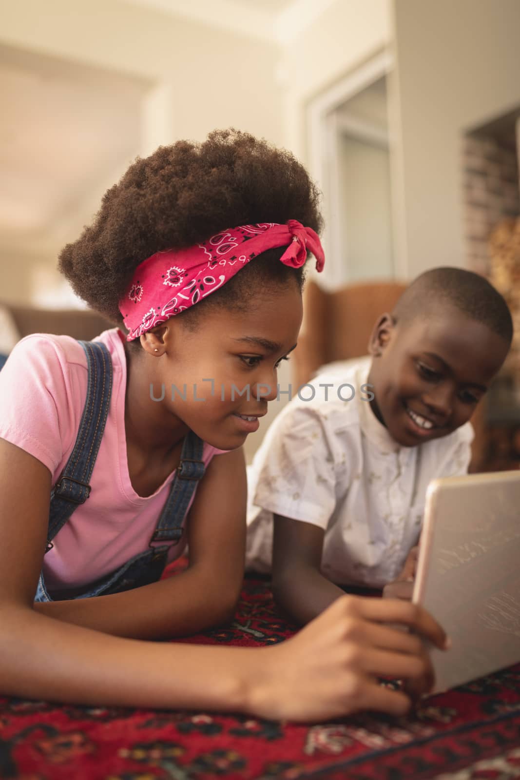 Close-up of African American sibling lying on floor, amusing and using digital tablet at home