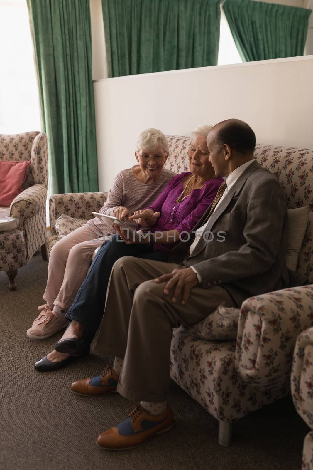 Front view of senior friends discussing over digital tablet while sitting on sofa at home