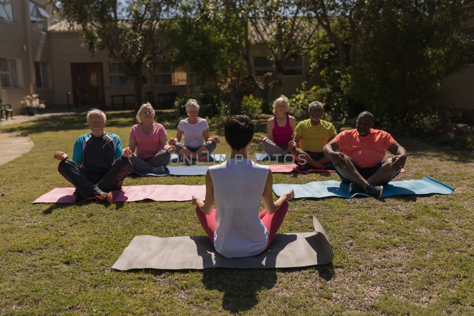 Front view of female trainer training senior people in performing yoga with yoga mat at park