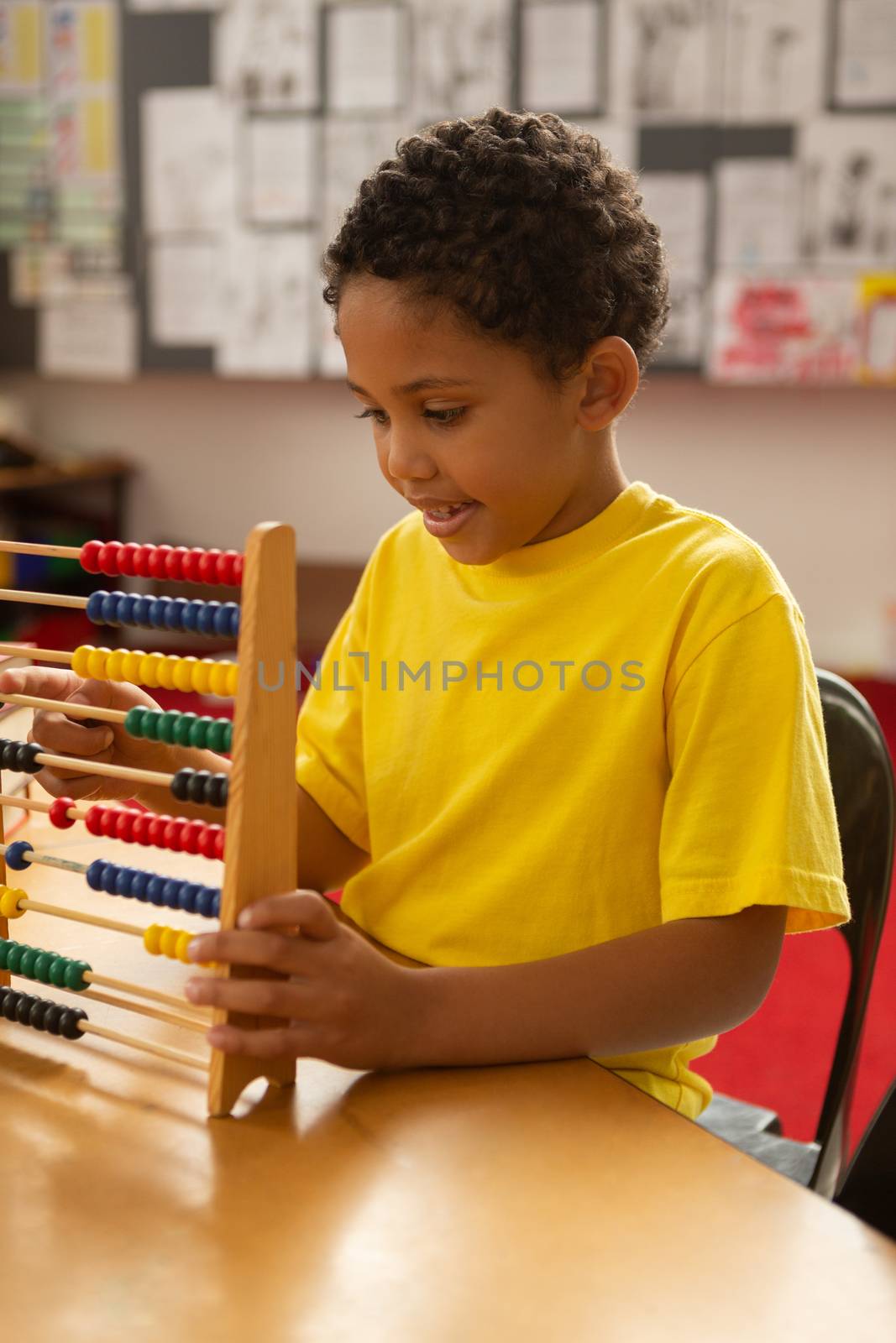 Front view of cute mixed-race schoolboy learning mathematics with abacus in a classroom at elementary school
