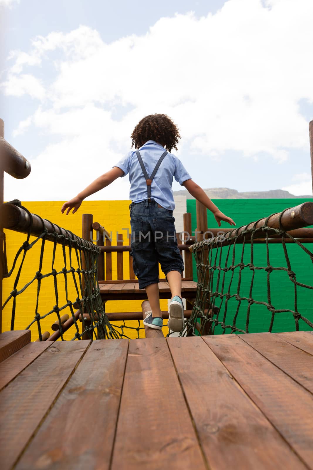 Rear view of a mixed-race schoolgirl walking on the net bridge in the school playground on a sunny day