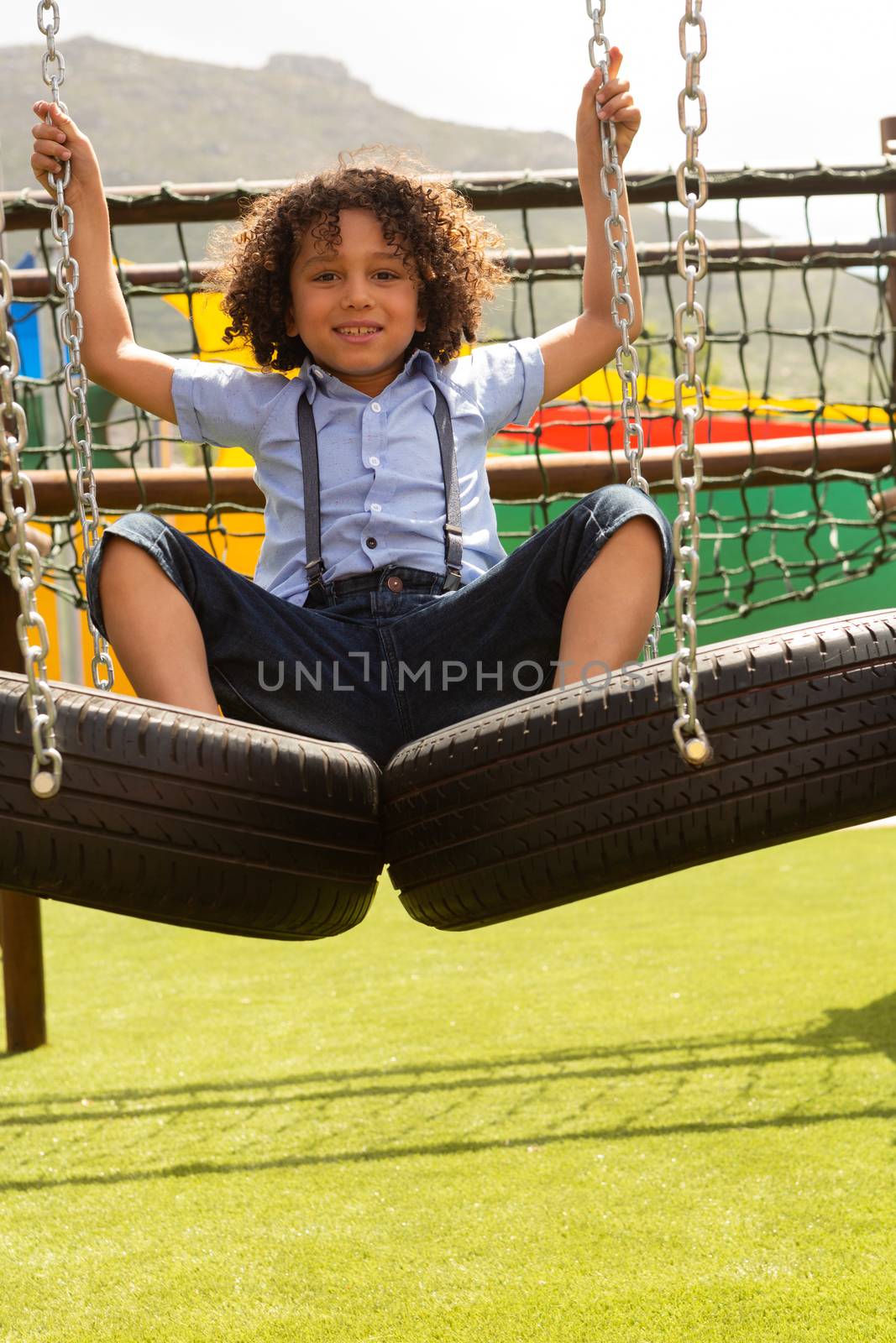 Front view of a mixed-race schoolgirl looking at the camera while playing on hanging tire in the school playground on a sunny day