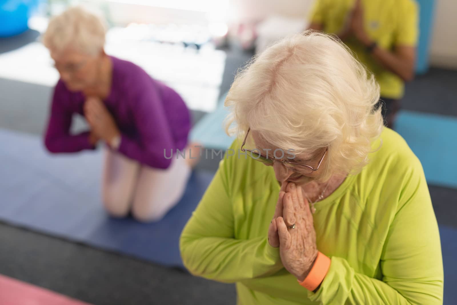 Front view of senior woman doing yoga on the foreground and her friend behind her in fitness studio