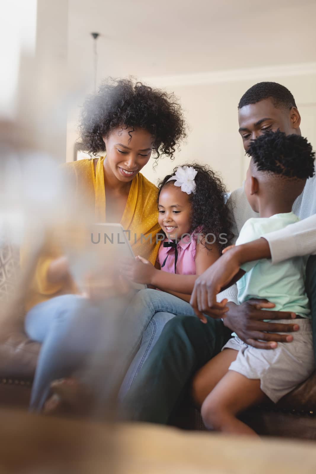 Front view of happy African American parents with their cute children using digital tablet on sofa in a comfortable home