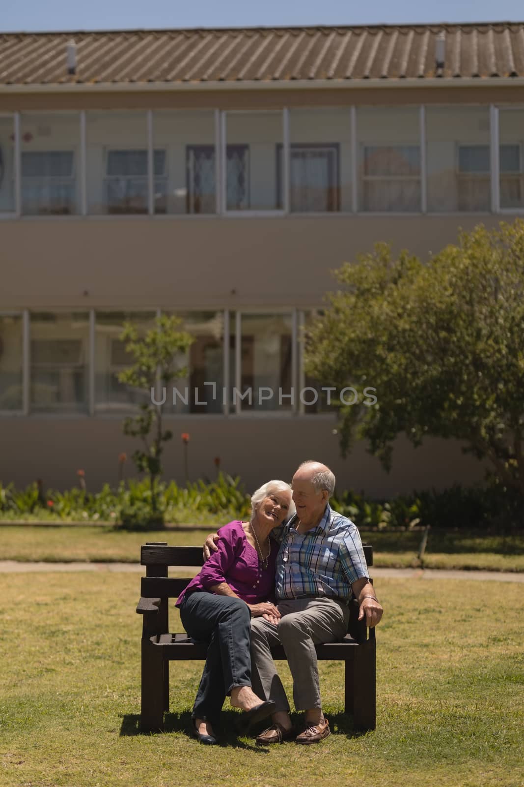 Front view of active senior couple sitting together and doing cuddle on the bench in the park