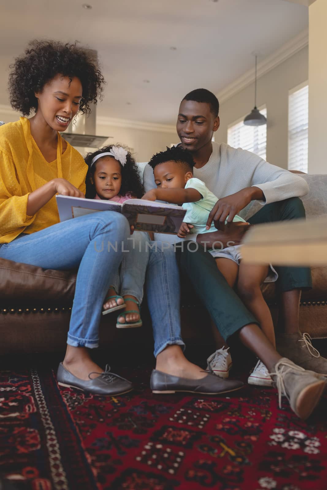 Happy African American parents with their cute children reading storybook on the sofa by Wavebreakmedia
