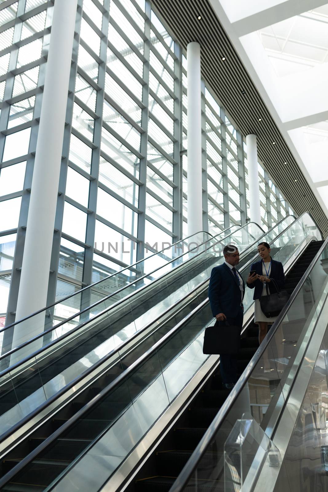 Businessman and businesswoman interacting with each other while moving down on escalator by Wavebreakmedia
