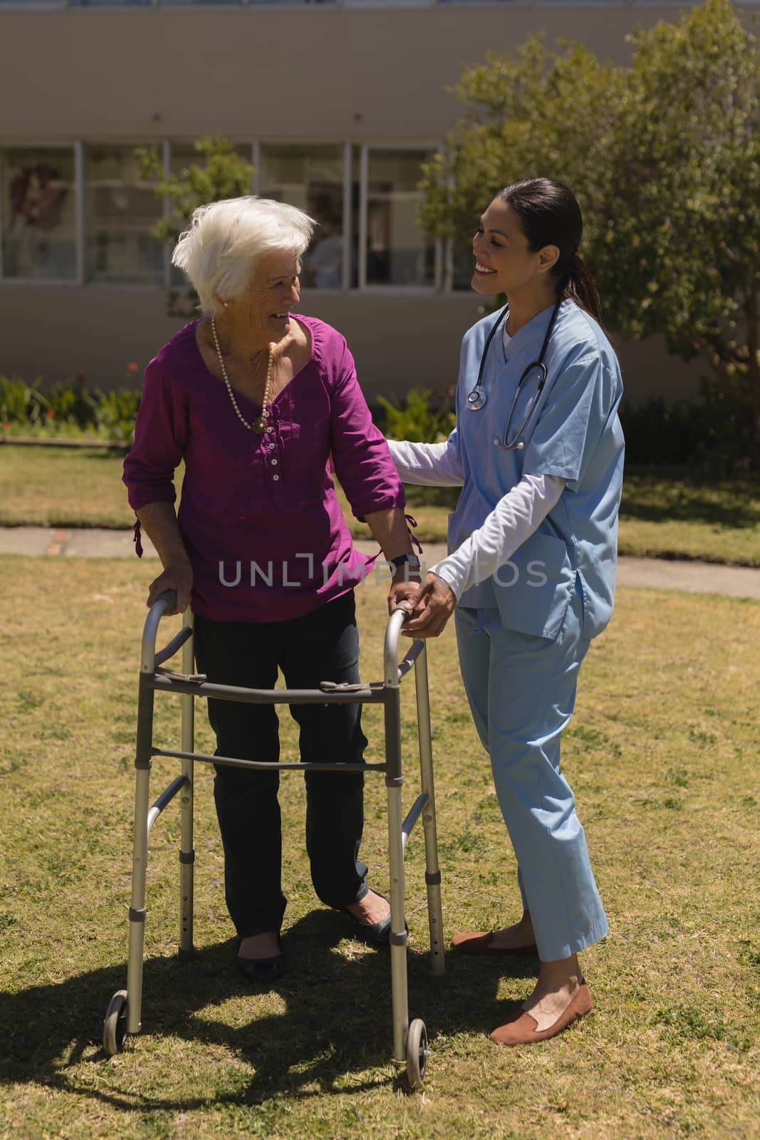 Front view of young female doctor helping disabled senior woman in garden on sunny day