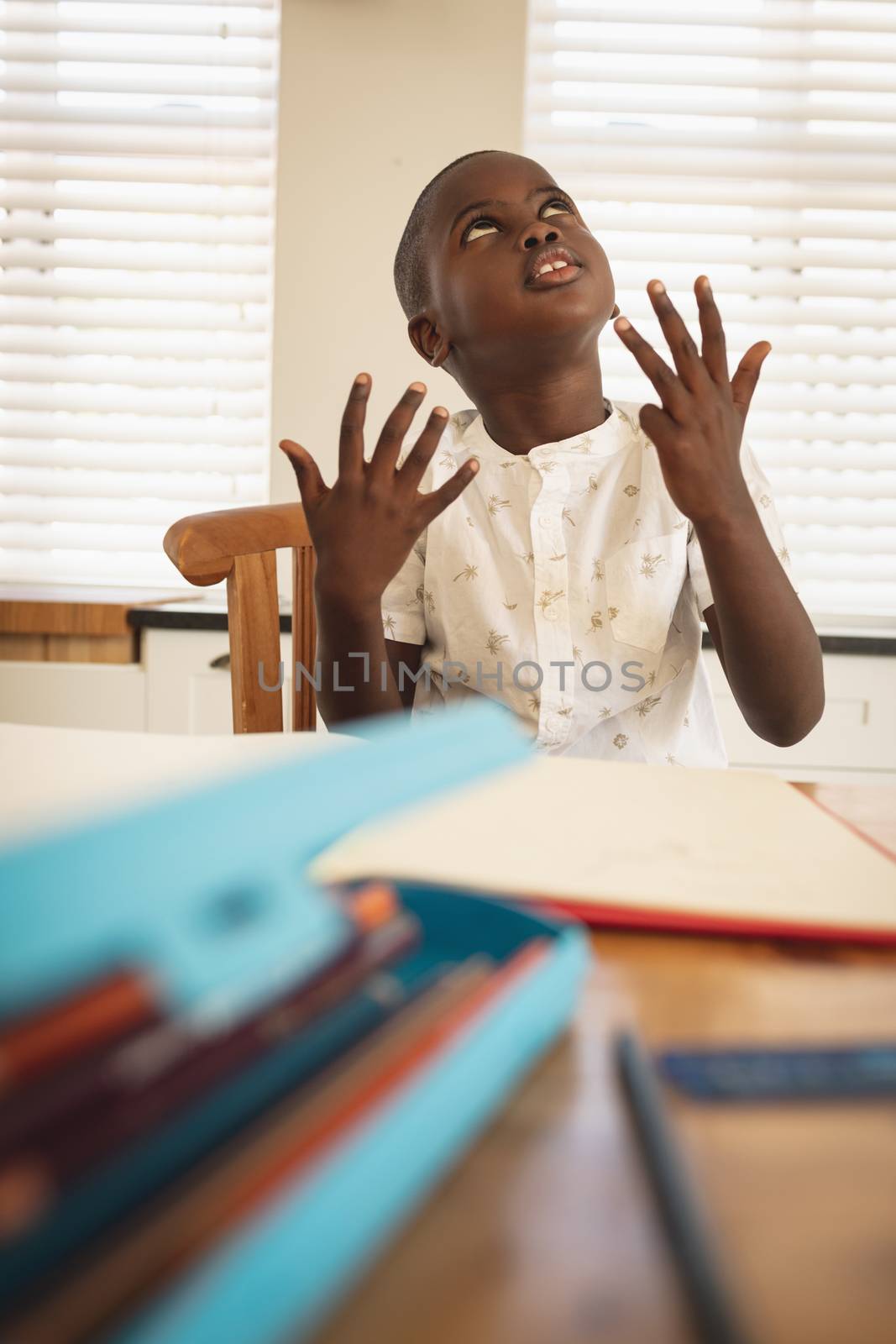 Front view of thoughtful African American boy doing homework on dining table in kitchen at home