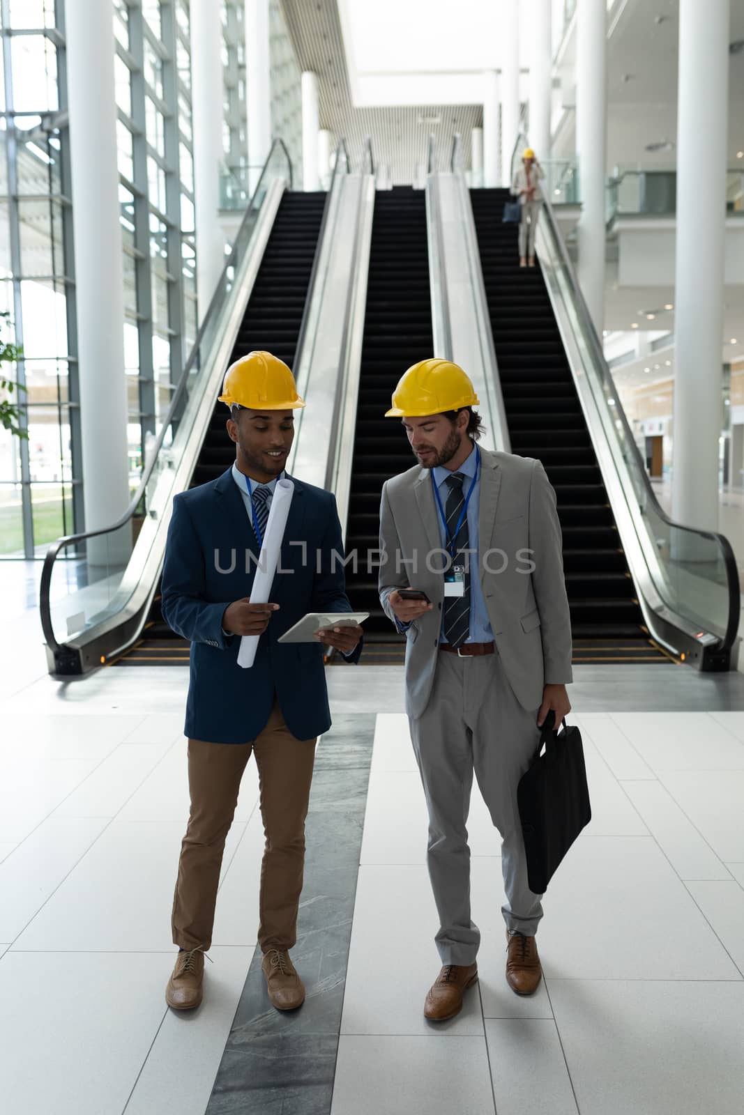 Front view of young multi-ethnic male architect discussing over digital tablet standing in office lobby