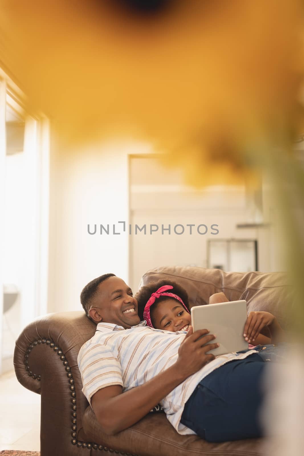 Happy African American father and daughter relaxing on the sofa and using digital table by Wavebreakmedia