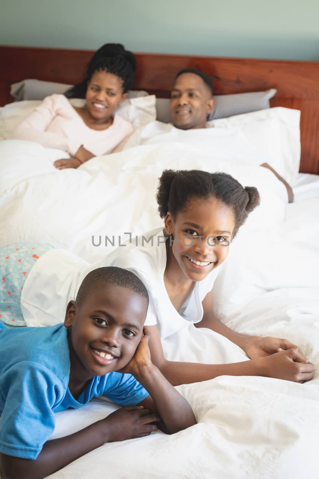 Happy African American family looking at camera while relaxing on bed in bedroom by Wavebreakmedia