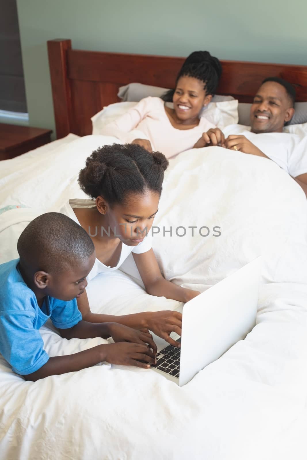 High angle view of African American children using laptop while parents relaxing on bed in bedroom at home