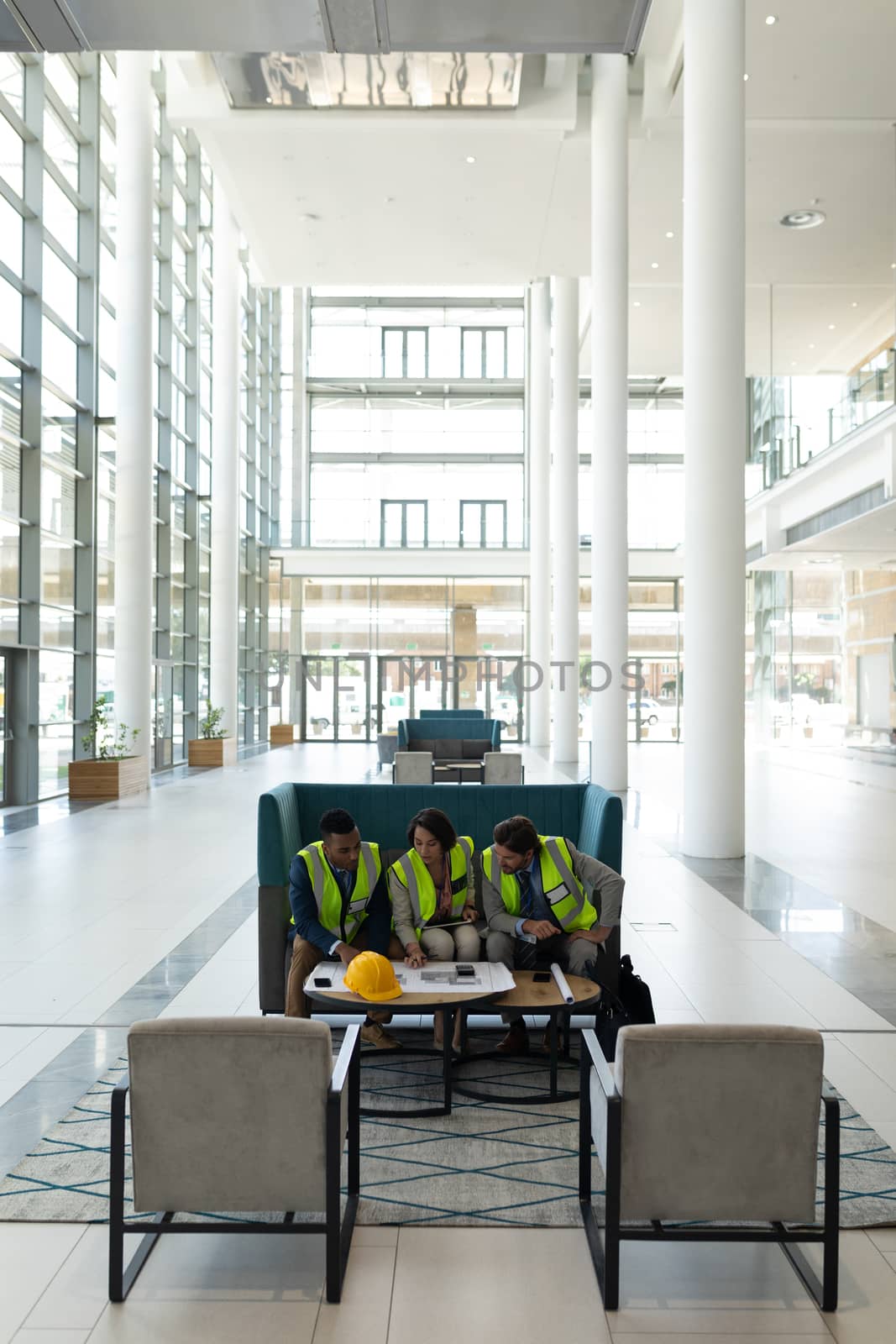 Front view of young multi-ethnic business architect sitting and discussing over the blue print in lobby at office