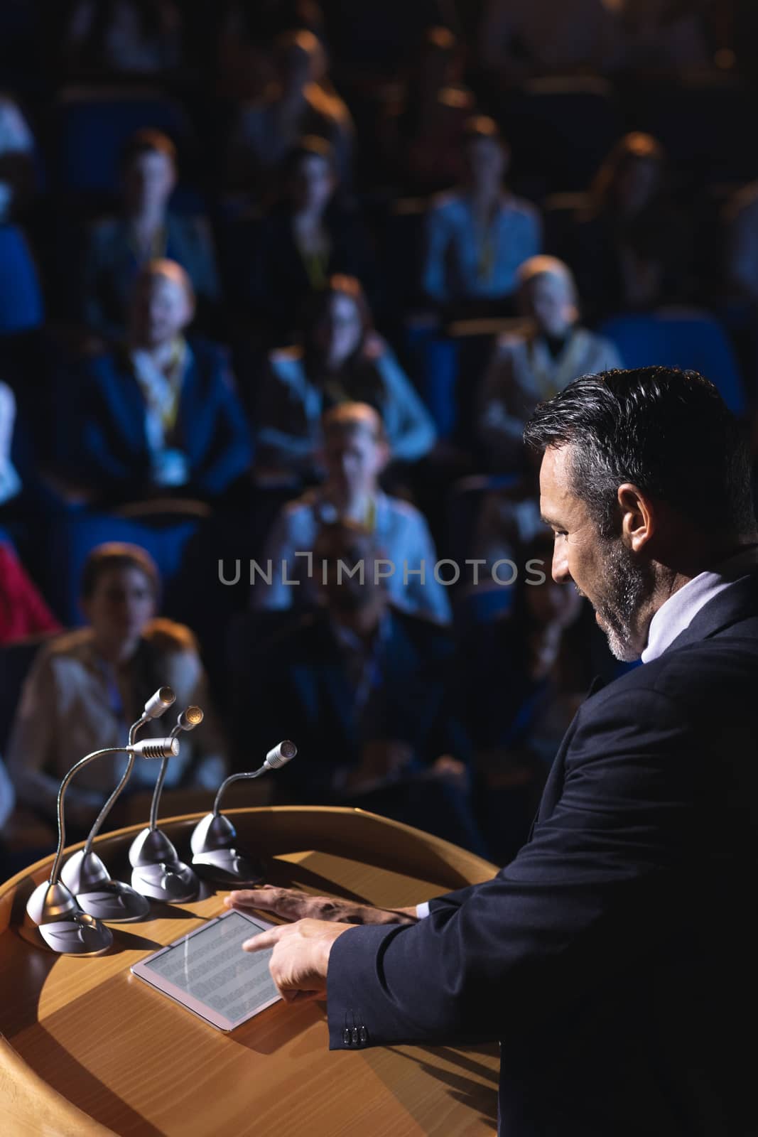 Businessman standing and looking at digital tablet on stage in auditorium by Wavebreakmedia