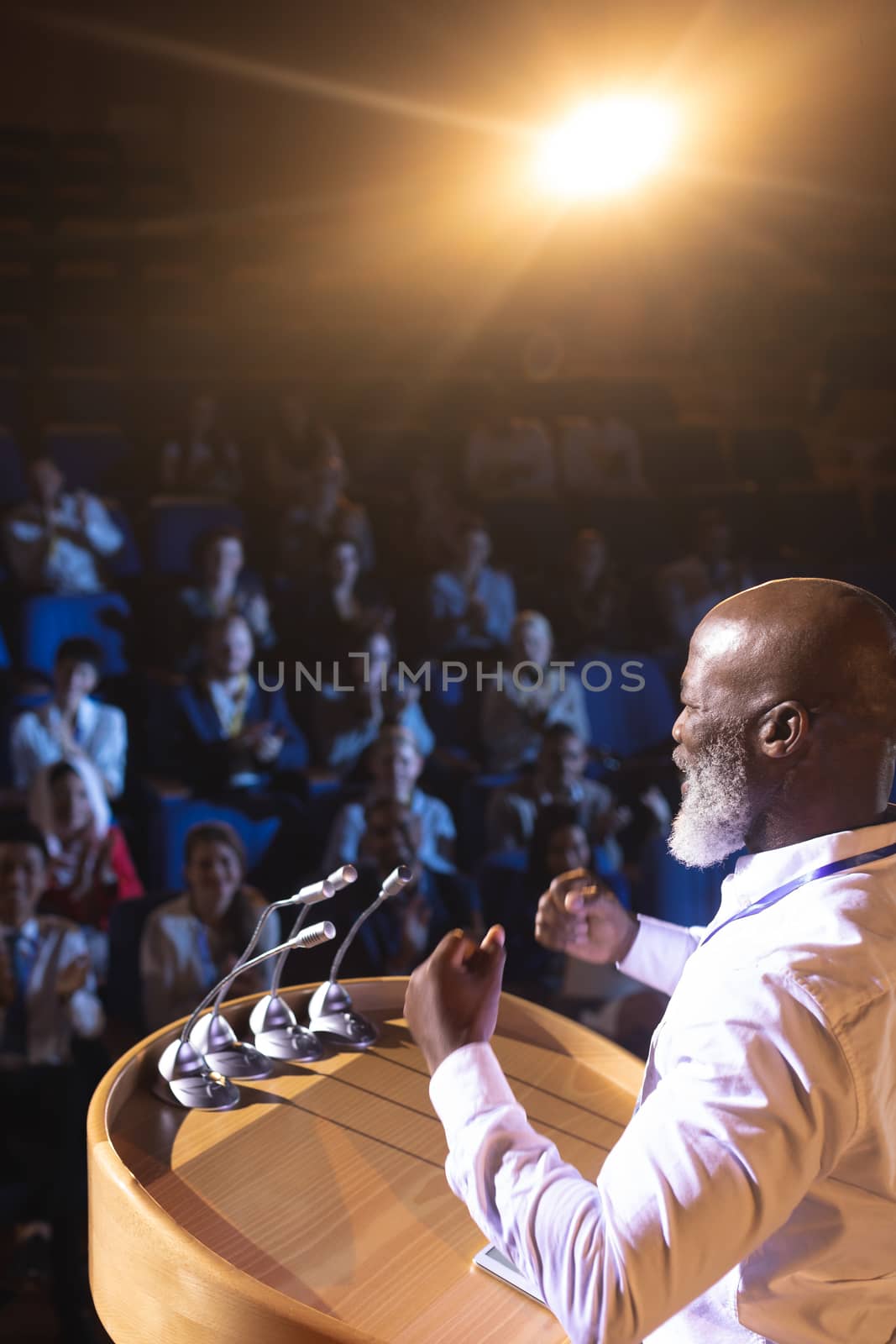 Businessman standing near podium and giving speech to the audience in the auditorium by Wavebreakmedia