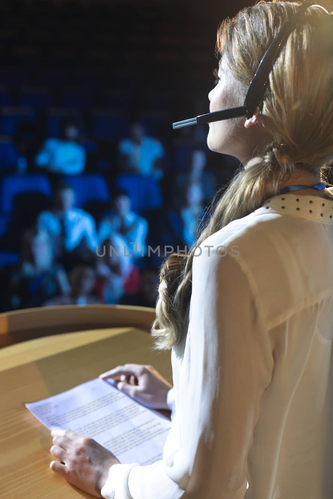 Rear view of young Caucasian businesswoman in headset giving presentation in the auditorium