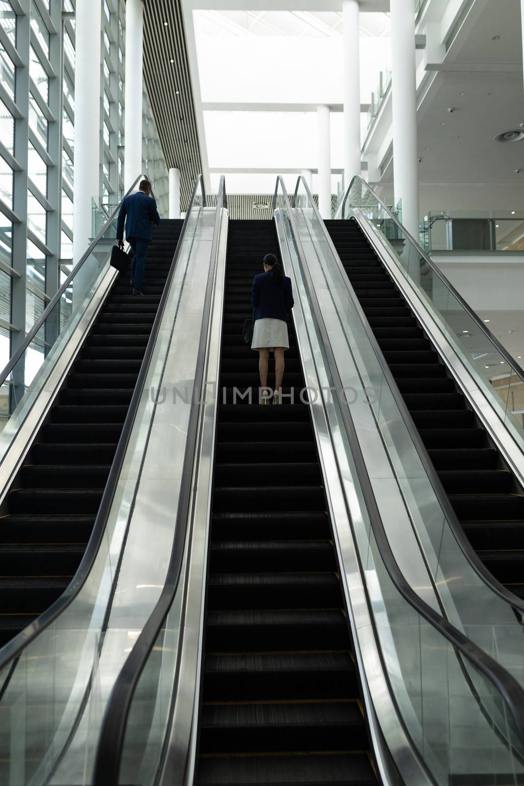 Businessman and businesswoman moving upwards on escalator in office lobby by Wavebreakmedia