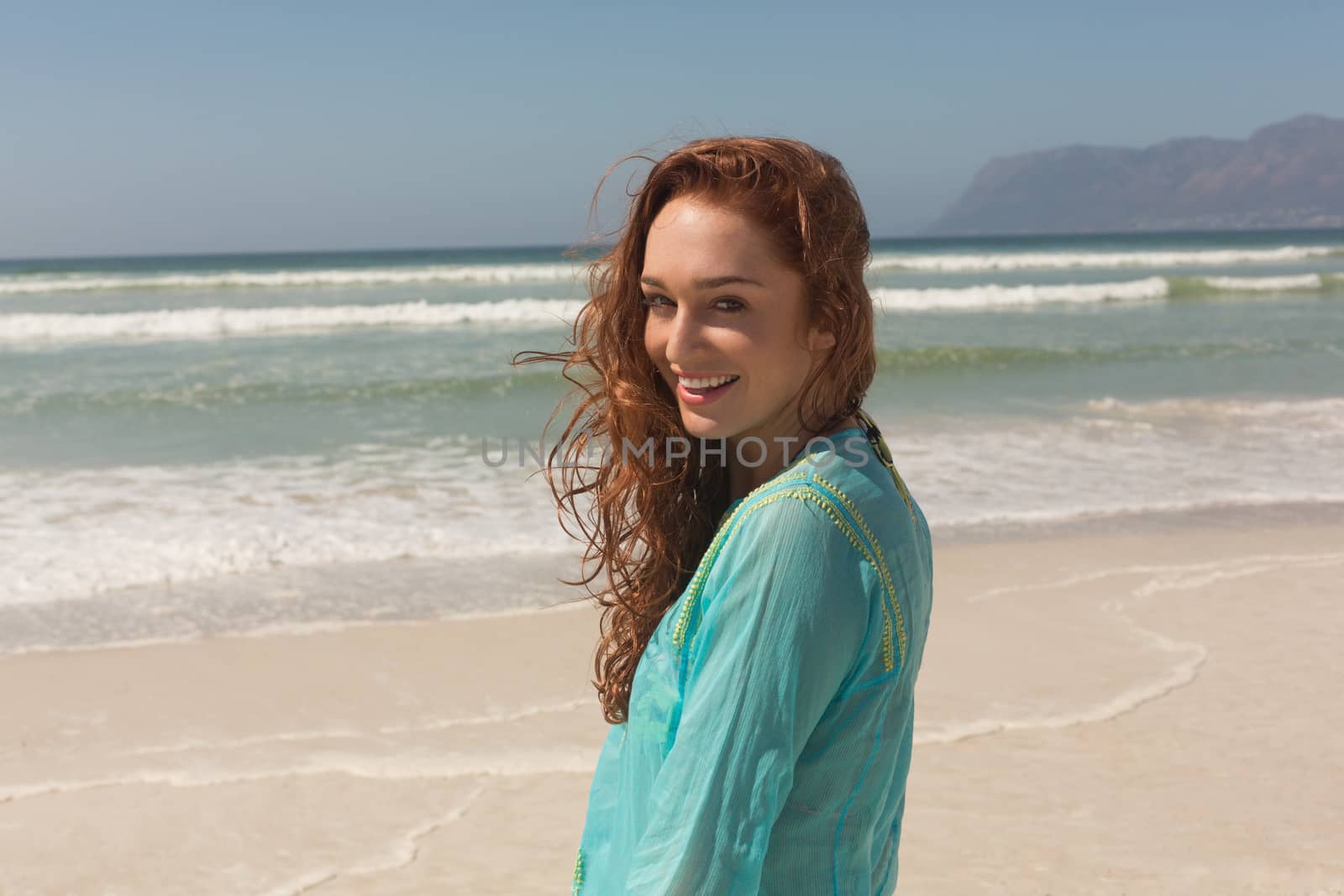 Portrait of happy beautiful young woman looking at camera standing on the beach. She is smiling